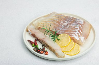 Çiğ pollock (Pollachius virens) fileto. Sağlıklı yaşam tarzı için taze balık. Limon, biberiye, deniz tuzu, kırmızı biber, karabiber. Hafif taş arkaplan, düz yatış, kopyalama alanı