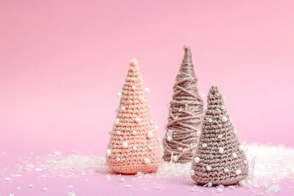 Handmade winter composition. Set of crocheted Christmas trees, artificial snow on pink background. Creative hobby concept, top view