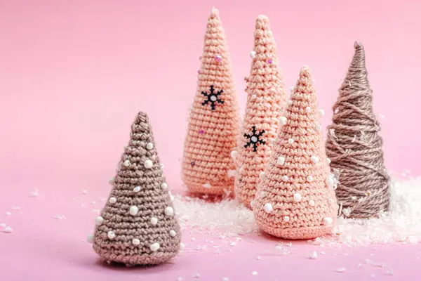 Handmade winter composition. Set of crocheted Christmas trees, artificial snow on pink background. Creative hobby concept, top view