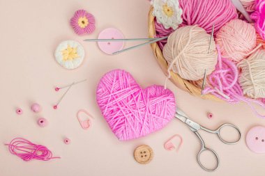 El yapımı bahar dekoru konsepti. Yaratıcı tığ işi, geleneksel çiçekler ve pembe bir kalp. Kutlama kartı, yumuşak pastel kayısı arkaplan, üst manzara.