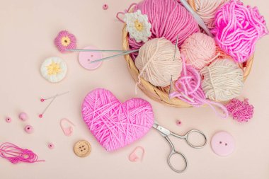 El yapımı bahar dekoru konsepti. Yaratıcı tığ işi, geleneksel çiçekler ve pembe bir kalp. Kutlama kartı, yumuşak pastel kayısı arkaplan, üst manzara.