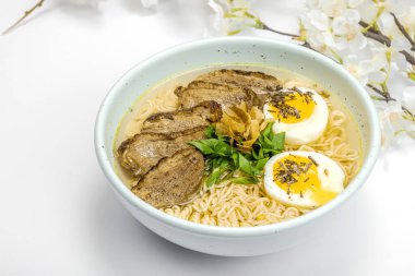 Japon eriştesi çorbalı Ramen. Sıcak yemek, ördek, yumurta, yeşillik. Beyaz arkaplan, kiraz çiçekleri, düz döşeme, kopyalama alanı