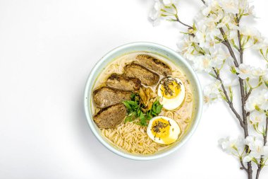 Japon eriştesi çorbalı Ramen. Sıcak yemek, ördek, yumurta, yeşillik. Beyaz arka plan, kiraz çiçekleri, düz yatak, üst manzara