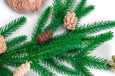 Yaratıcı el yapımı kış yatağı. Sıcak örülü çam kozalakları, geleneksel dekor, aletler, el işi ruh hali konsepti. Beyaz arka plan, yemyeşil Noel ağacı dalı, üst manzara