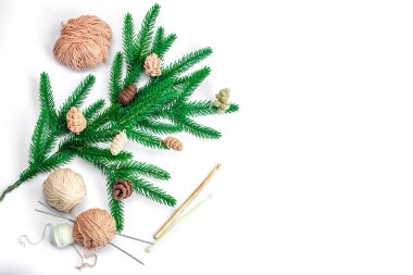 Yaratıcı el yapımı kış yatağı. Sıcak örülü çam kozalakları, geleneksel dekor, aletler, el işi ruh hali konsepti. Beyaz arka plan, yemyeşil Noel ağacı dalı, üst manzara