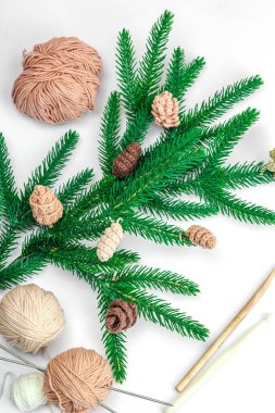 Yaratıcı el yapımı kış yatağı. Sıcak örülü çam kozalakları, geleneksel dekor, aletler, el işi ruh hali konsepti. Beyaz arka plan, yemyeşil Noel ağacı dalı, üst manzara