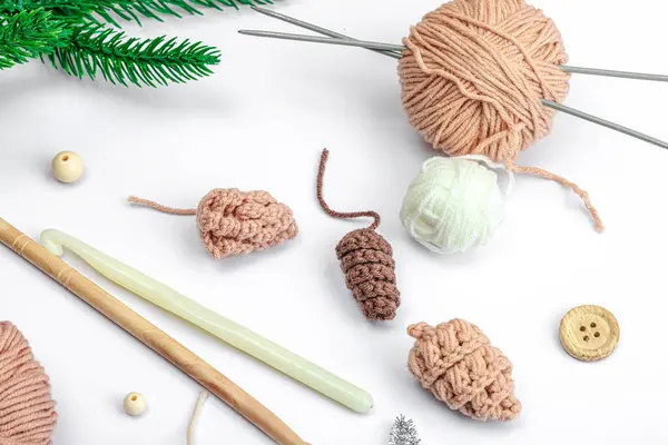 Creative handmade winter flat lay. Cozy crocheted pine cones, traditional decor, tools, craft mood concept. White background, evergreen Christmas tree branch, top view