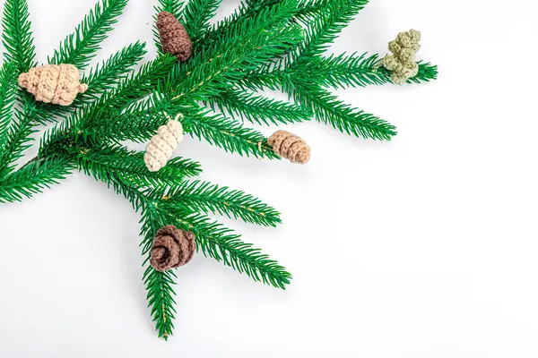 Cozy crocheted pine cones on evergreen Christmas tree branch. Creative handmade decor, craft mood concept. White background, winter flat lay, top view