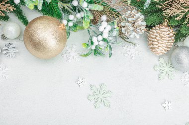 Geleneksel yeni yıl kompozisyonu. Şenlikli dekor, karlı Noel ağacı dalları, takılar, kozalaklar. Hafif taş arkaplan, üst görünüm