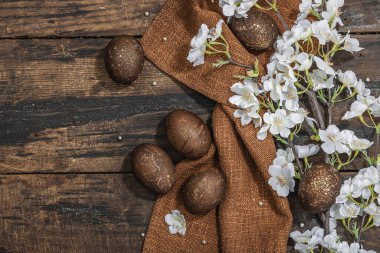 Paskalya yumurtaları ve koyu ahşap arka planda çiçek açan kiraz dalları. Kutlama konsepti, tebrik kartı, düz konum, sert ışık, koyu gölge, üst görünüm