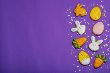 Geleneksel Paskalya kurabiyeleri, yenilebilir şenlik dekorları. Ev yapımı pişirme konsepti, tatlı tatlılar. Tebrik kartı, mor arkaplan, düz yatak, üst görünüm