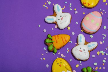 Geleneksel Paskalya kurabiyeleri, yenilebilir şenlik dekorları. Ev yapımı pişirme konsepti, tatlı tatlılar. Tebrik kartı, mor arkaplan, düz yatak, üst görünüm