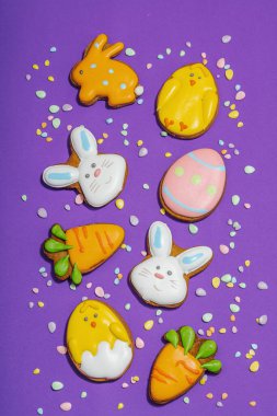 Geleneksel Paskalya kurabiyeleri, yenilebilir şenlik dekorları. Ev yapımı pişirme konsepti, tatlı tatlılar. Tebrik kartı, mor arkaplan, düz yatak, üst görünüm