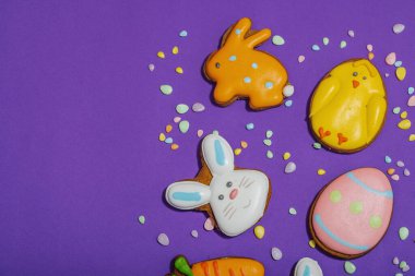 Geleneksel Paskalya kurabiyeleri, yenilebilir şenlik dekorları. Ev yapımı pişirme konsepti, tatlı tatlılar. Tebrik kartı, mor arkaplan, düz yatak, üst görünüm