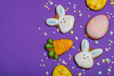 Geleneksel Paskalya kurabiyeleri, yenilebilir şenlik dekorları. Ev yapımı pişirme konsepti, tatlı tatlılar. Tebrik kartı, mor arkaplan, düz yatak, üst görünüm