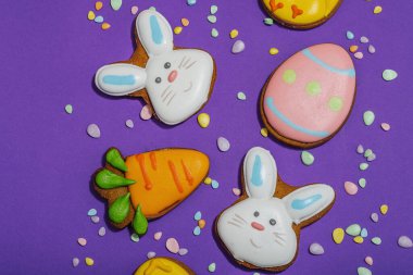 Geleneksel Paskalya kurabiyeleri, yenilebilir şenlik dekorları. Ev yapımı pişirme konsepti, tatlı tatlılar. Tebrik kartı, mor arkaplan, düz yatak, üst görünüm