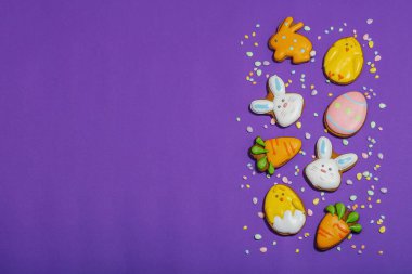 Geleneksel Paskalya kurabiyeleri, yenilebilir şenlik dekorları. Ev yapımı pişirme konsepti, tatlı tatlılar. Tebrik kartı, mor arkaplan, düz yatak, üst görünüm