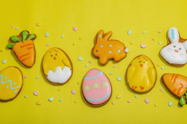 Geleneksel Paskalya kurabiyeleri, yenilebilir şenlik dekorları. Ev yapımı pişirme konsepti, tatlı tatlılar. Tebrik kartı, sarı arkaplan, düz yatak, üst manzara