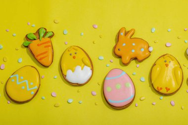Geleneksel Paskalya kurabiyeleri, yenilebilir şenlik dekorları. Ev yapımı pişirme konsepti, tatlı tatlılar. Tebrik kartı, sarı arkaplan, düz yatak, üst manzara