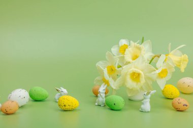 Paskalya yumurtalı nergisler ve açık yeşil arka planda tavşanlar. Mutlu bayramlar, tebrik kartı, geleneksel şenlik kompozisyonu, metin için yer