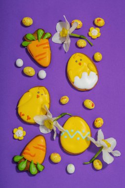 Geleneksel Paskalya kurabiyeleri, yenilebilir şenlik dekorları. Ev yapımı pişirme konsepti, tatlı tatlılar. Tebrik kartı, mor arkaplan, düz yatak, üst görünüm