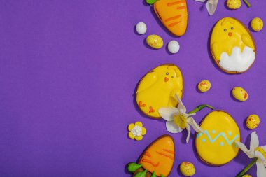 Geleneksel Paskalya kurabiyeleri, yenilebilir şenlik dekorları. Ev yapımı pişirme konsepti, tatlı tatlılar. Tebrik kartı, mor arkaplan, düz yatak, üst görünüm