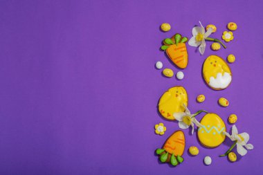 Geleneksel Paskalya kurabiyeleri, yenilebilir şenlik dekorları. Ev yapımı pişirme konsepti, tatlı tatlılar. Tebrik kartı, mor arkaplan, düz yatak, üst görünüm