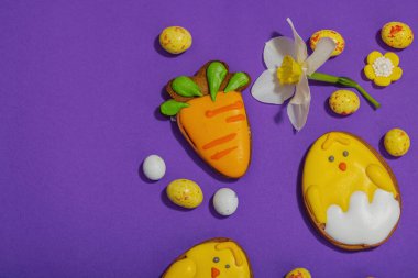 Geleneksel Paskalya kurabiyeleri, yenilebilir şenlik dekorları. Ev yapımı pişirme konsepti, tatlı tatlılar. Tebrik kartı, mor arkaplan, düz yatak, üst görünüm
