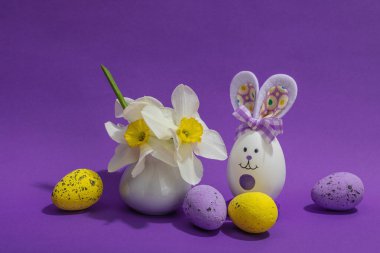 Çiçekli nergisler, paskalya yumurtaları ve mor arka planda tavşanlar. Mutlu bayramlar, tebrik kartı, geleneksel festival kompozisyonu, kopyalama alanı
