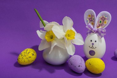 Çiçekli nergisler, paskalya yumurtaları ve mor arka planda tavşanlar. Mutlu bayramlar, tebrik kartı, geleneksel şenlik kompozisyonu, kapatın.
