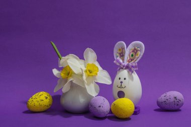 Çiçekli nergisler, paskalya yumurtaları ve mor arka planda tavşanlar. Mutlu bayramlar, tebrik kartı, geleneksel festival kompozisyonu, kopyalama alanı