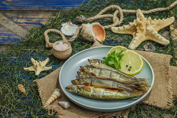Smoked smelt with fresh lemon and herbs. Salted fish with marine decor. Trendy dish, sea rope. Blue nautical wooden background, copy space