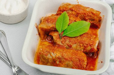 Pirinçle doldurulmuş lahana ruloları ve domates sosunda pişirilmiş et. Geleneksel yemek, hazır yemek, ekşi krema. Hafif taş arkaplan, kapat