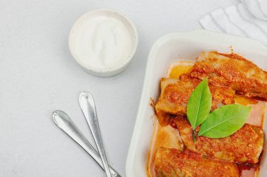 Pirinçle doldurulmuş lahana ruloları ve domates sosunda pişirilmiş et. Geleneksel yemek, hazır yemek, ekşi krema. Hafif taş arkaplan, üst görünüm