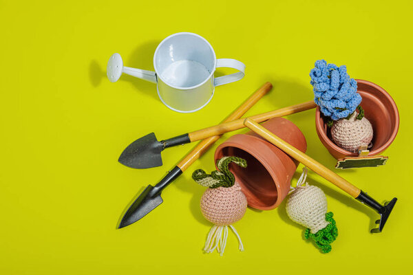Spring planting and gardening concept. Handmade flowers with bulbs, mini tools, watering can, and buckets. Hard light, dark shadow, bright yellow background, top view