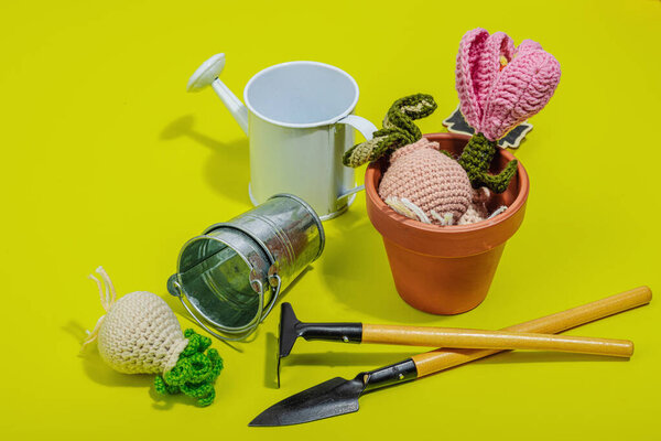 Spring planting and gardening concept. Handmade flowers with bulbs, mini tools, watering can, and buckets. Hard light, dark shadow, bright yellow background, close up