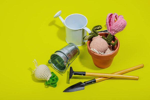 Spring planting and gardening concept. Handmade flowers with bulbs, mini tools, watering can, and buckets. Hard light, dark shadow, bright yellow background, copy space