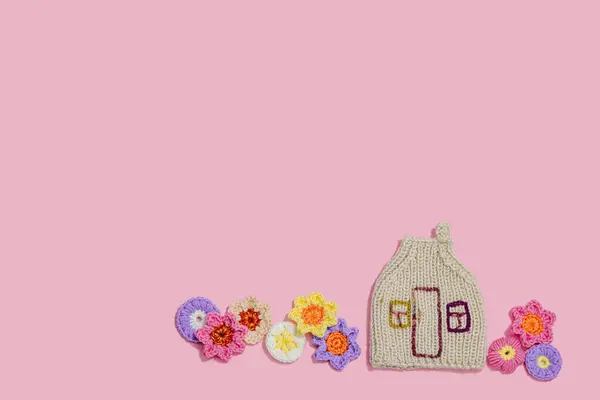 Handmade home spring decor concept. Creative crocheting, house figurine, traditional flowers. Festive greeting card, gentle pastel pink background, top view