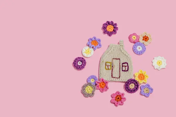 Handmade home spring decor concept. Creative crocheting, house figurine, traditional flowers. Festive greeting card, gentle pastel pink background, top view