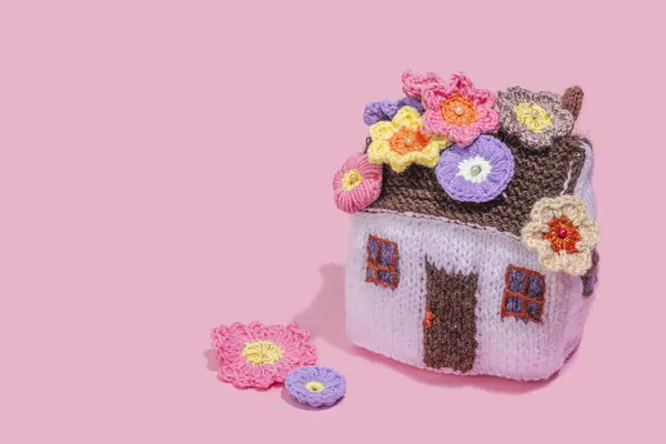 Handmade home spring decor concept. Creative crocheting, house figurine, traditional flowers. Festive greeting card, gentle pastel pink background, copy space