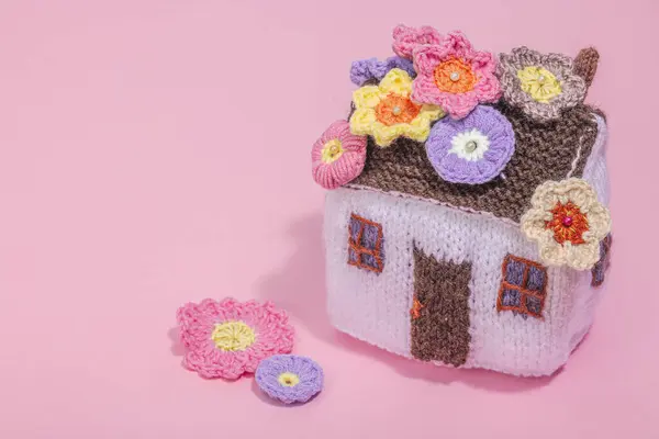 Handmade home spring decor concept. Creative crocheting, house figurine, traditional flowers. Festive greeting card, gentle pastel pink background, copy space