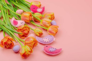 Nazik Paskalya kompozisyonu lale çiçekleri ve el yapımı keçeli kuşlar. Geleneksel dekoratif unsurlar, tebrik kartı. Düz konum, pembe arkaplan, kopyalama alanı