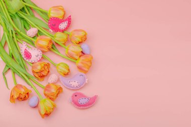 Nazik Paskalya kompozisyonu lale çiçekleri ve el yapımı keçeli kuşlar. Geleneksel dekoratif unsurlar, tebrik kartı. Düz yatış, pembe arkaplan, üst görünüm