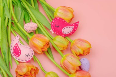 Nazik Paskalya kompozisyonu lale çiçekleri ve el yapımı keçeli kuşlar. Geleneksel dekoratif unsurlar, tebrik kartı. Düz yatış, pembe arkaplan, üst görünüm