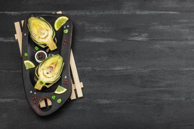 Ahşap arka planda pişen taze yeşil enginarlar. Sağlıklı vejetaryen yiyecekler için geleneksel mevsimlik malzemeler, düz yatak. Baharatlar, yeşiller, limon dilimleri, üst manzara