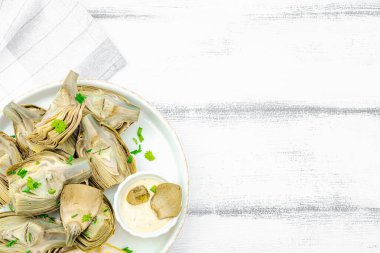 Geleneksel İtalyan enginarı, pişmiş karsiofi sebzesi. Zeytinyağı, sarımsak, maydanoz ve limon. Beyaz ahşap arka plan, baharatlı sos, yakın plan.