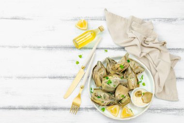 Geleneksel İtalyan enginarı, pişmiş karsiofi sebzesi. Zeytinyağı, sarımsak, maydanoz ve limon. Beyaz ahşap arka plan, baharatlı sos, üst manzara.