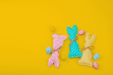 El yapımı Paskalya konsepti. Geleneksel dekorasyonlu tekstil tavşanları dikmek. Kutlama sembolleri, tebrik kartları, düz yatış. Yaratıcı zanaat konsepti, parlak sarı arka plan, üst görünüm