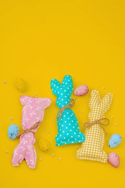 El yapımı Paskalya konsepti. Geleneksel dekorasyonlu tekstil tavşanları dikmek. Kutlama sembolleri, tebrik kartları, düz yatış. Yaratıcı zanaat konsepti, parlak sarı arka plan, üst görünüm