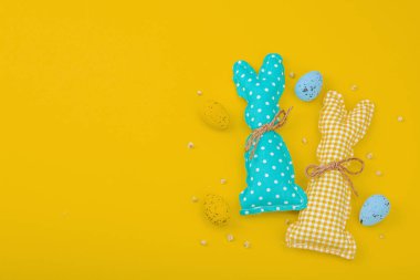 El yapımı Paskalya konsepti. Geleneksel dekorasyonlu tekstil tavşanları dikmek. Kutlama sembolleri, tebrik kartları, düz yatış. Yaratıcı zanaat konsepti, parlak sarı arka plan, üst görünüm